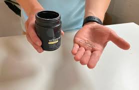 A person holding a dark bottle of vitamins in one hand and three clear capsules in the palm of the other hand