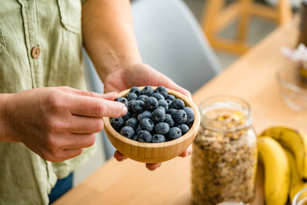 A person's hands holding a small wooden bowl overflowing with fresh, ripe blueberries